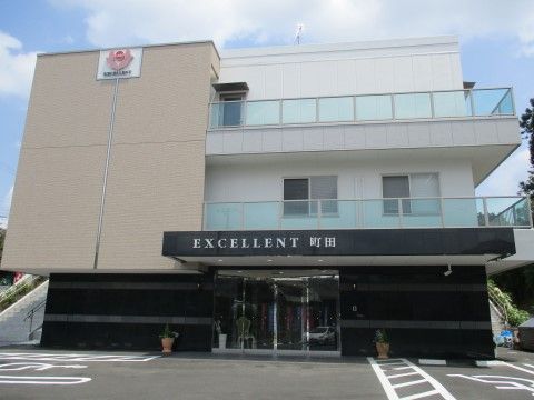 ３階建ての建物で一階とひさしが黒く、他はベージュと白の外観である。2〜３階にはガラスのフェンスがついたベランダがある。