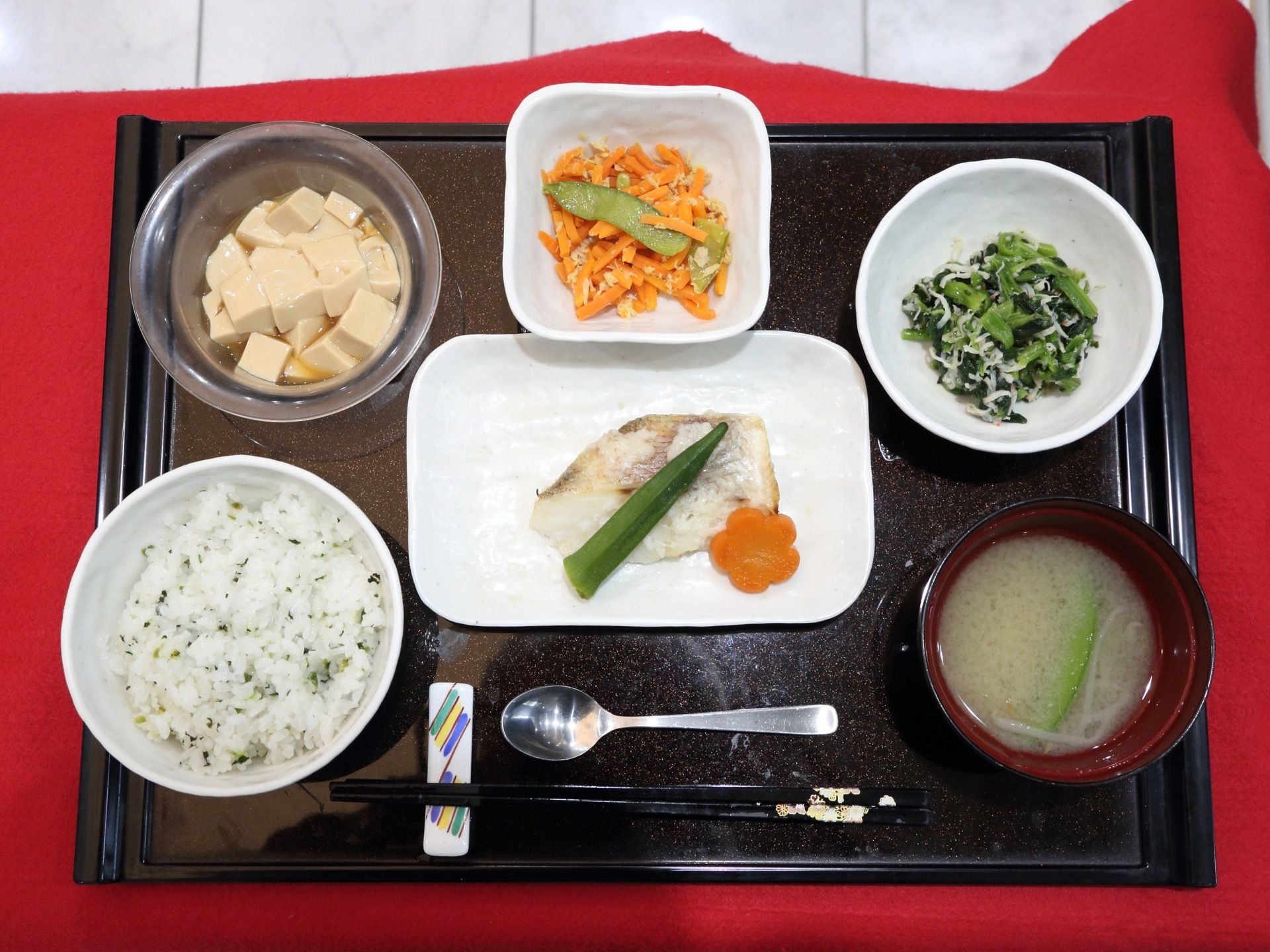 献立の一例をあげると、青菜ご飯、味噌汁、白身魚の酒蒸し、豆腐のおひたし、にんじんしりしり、青菜としらすの和え物である。