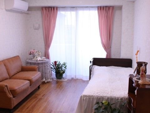 突き当りが掃き出し窓で、向かって右側の壁際にベッドがある。左側には２人掛けのソファがある。間は充分に空いている。