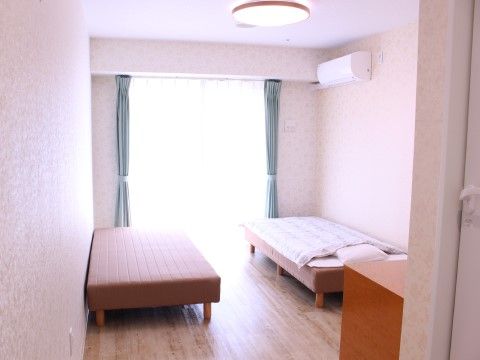 突き当りが掃き出し窓で、両側の壁に一台シングルベッドが置かれている。エアコン付きで、部屋に無駄な装飾がない。