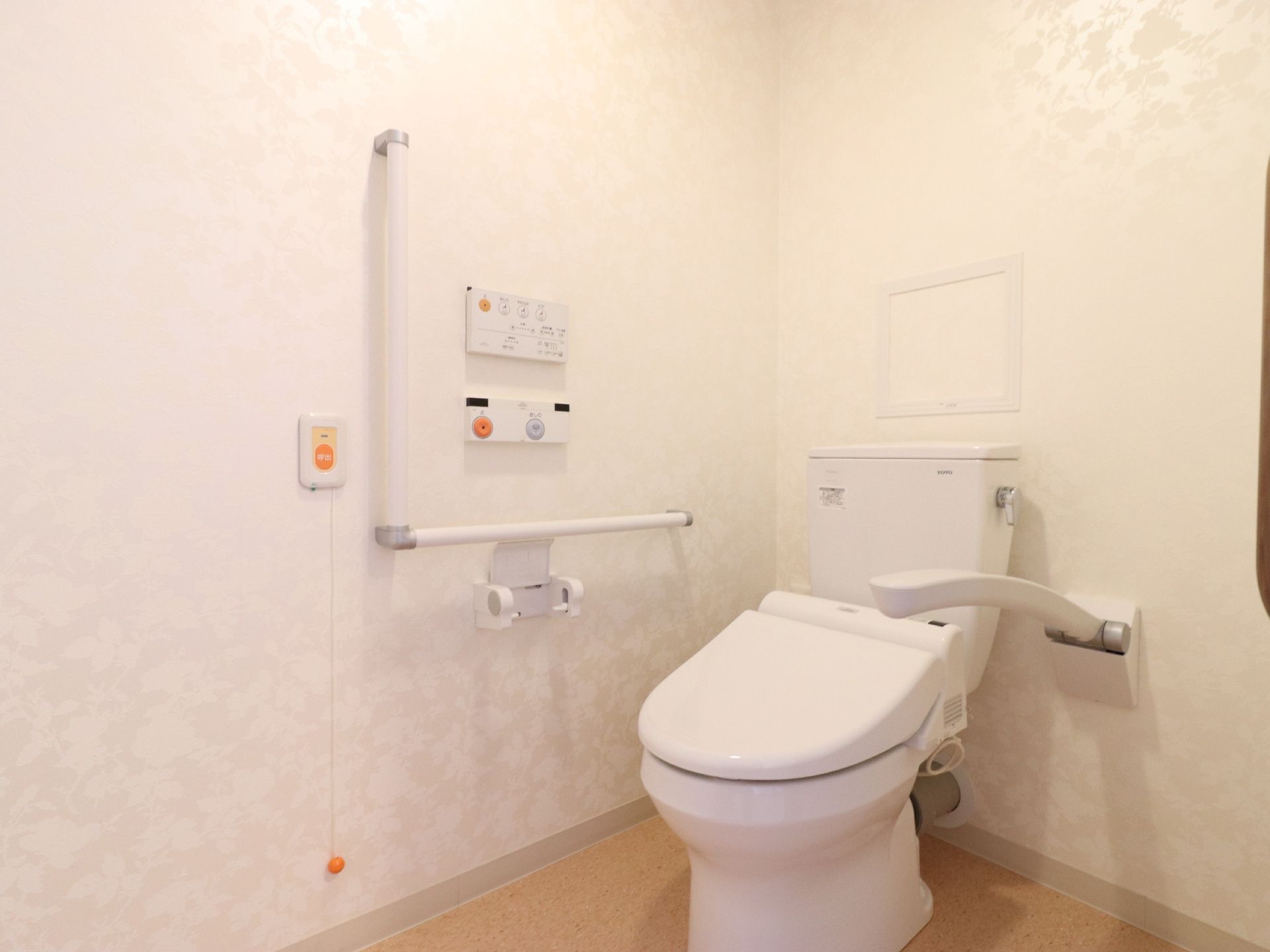 水を流す等は、壁に設置されているパネルで操作が可能。トイレットペーパーホルダーが一つある。壁紙は白で明るい。