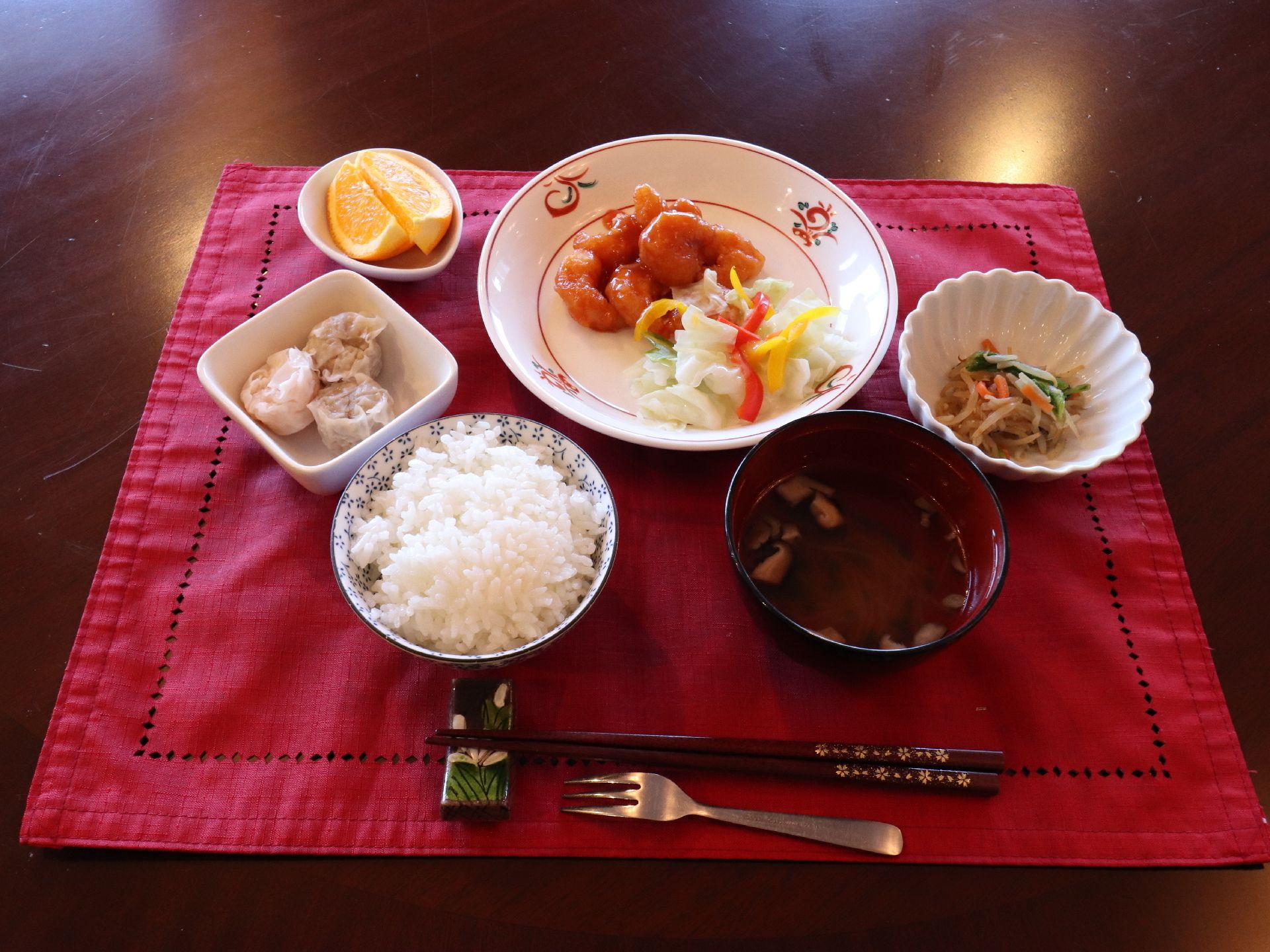 好みが分かれにくい中華の食事。敷物が敷かれている。彩り豊かに食事が盛られている。口をさっぱりとさせるデザート付き。