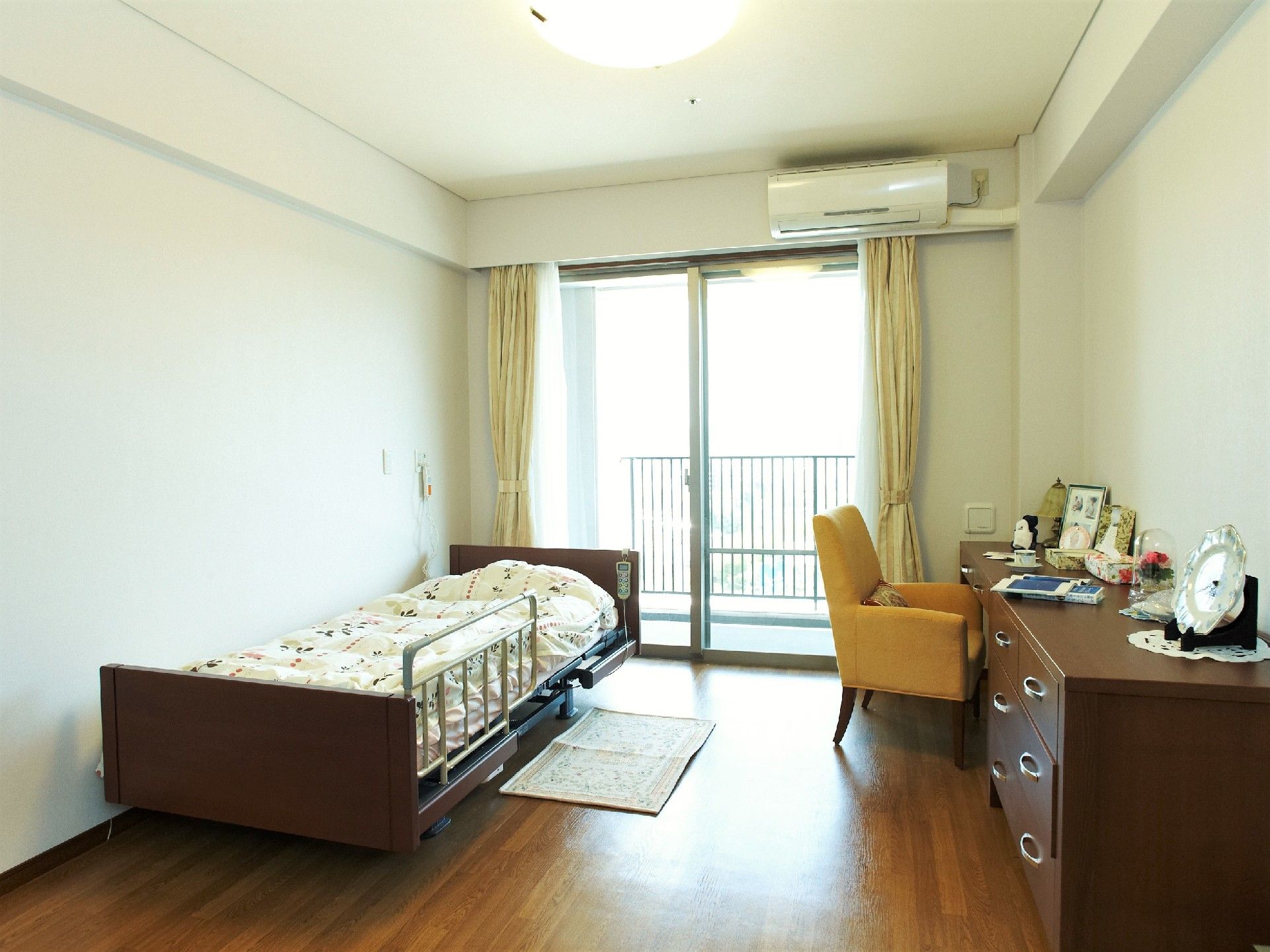 フローリング張りの部屋に介護ベッドとチェストが置かれている。奥にはオレンジ色の椅子も見える