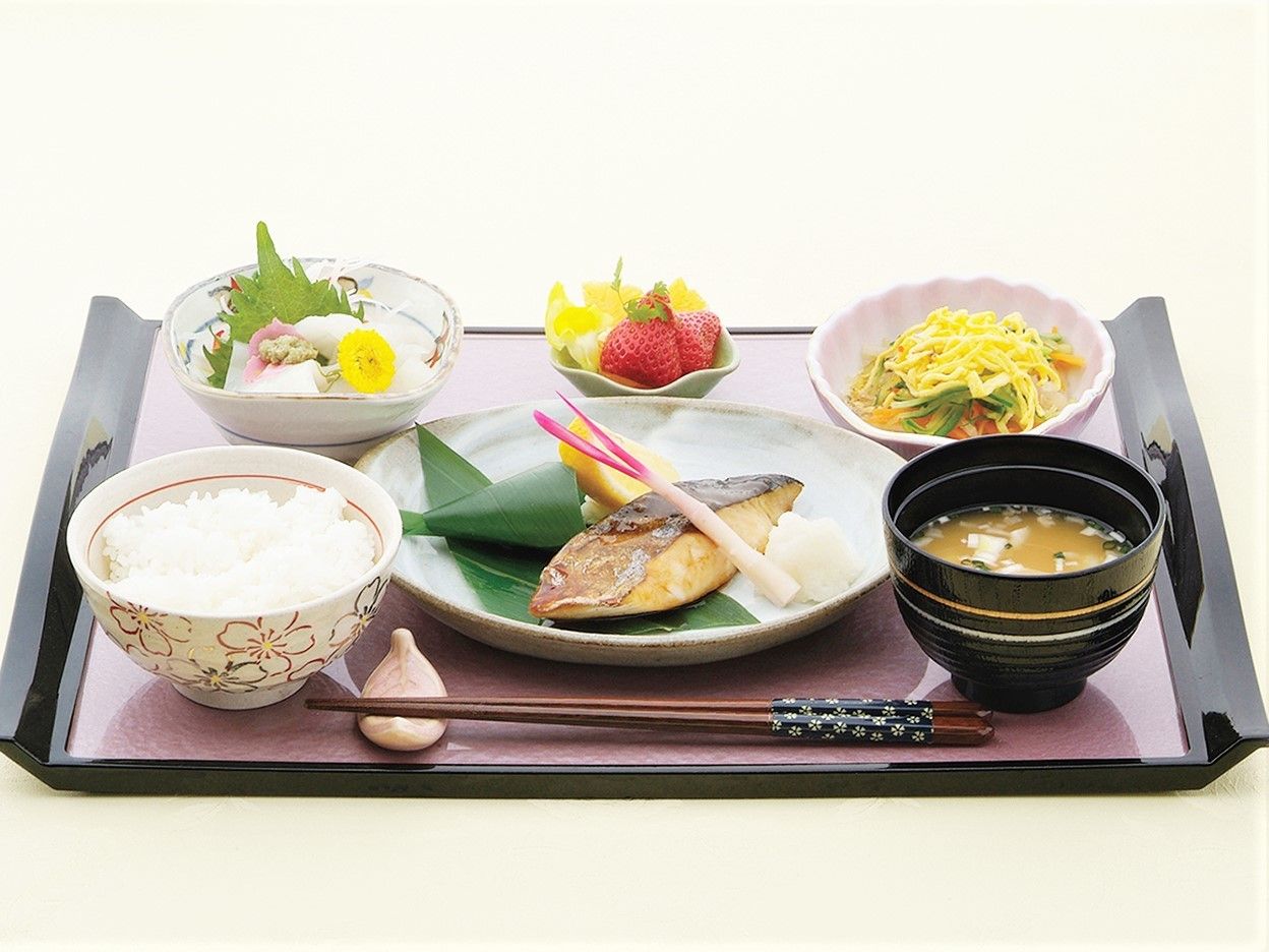 黒いお盆の上に、ご飯、お味噌汁、焼き魚、お刺身等が載っている