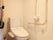 温水洗浄便座が1台置かれた個室のトイレで、壁側に固定された手すりが、反対側に可動式の手すりが設置されている。