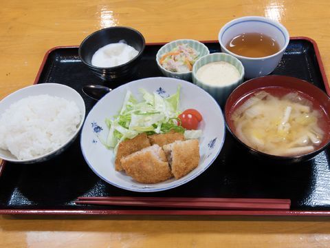 黒いお盆に7点食器が盛り付けてある。スプーンと箸が1膳分そえてある。メイン惣菜には野菜がそえてあるほか、小鉢にも野菜が盛り付けてある。
