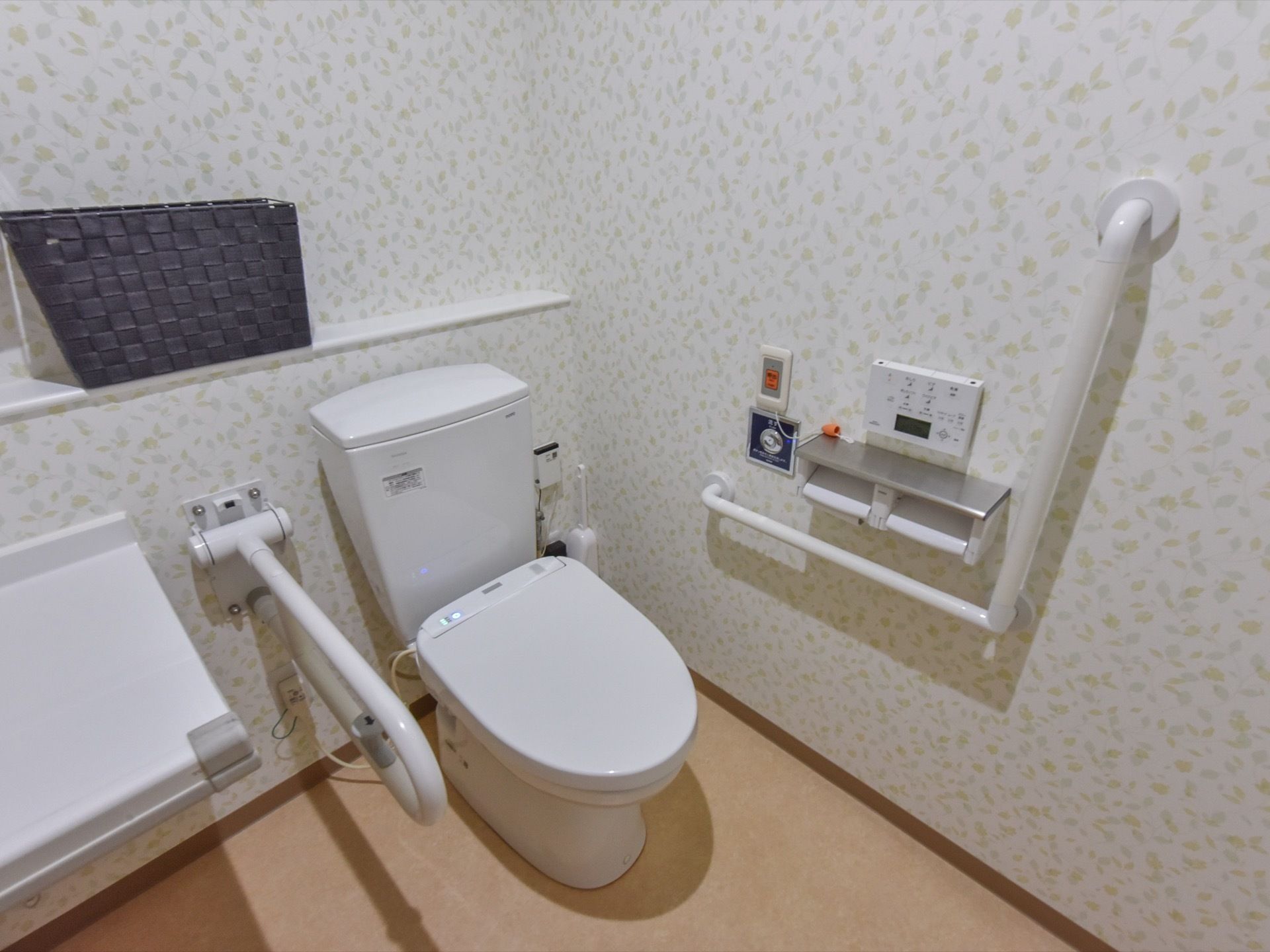 広くて清潔なスペースに、白い便器が設置されている。便器には温水洗浄便座が備わっている。壁側に温度調節などの操作パネルがある。