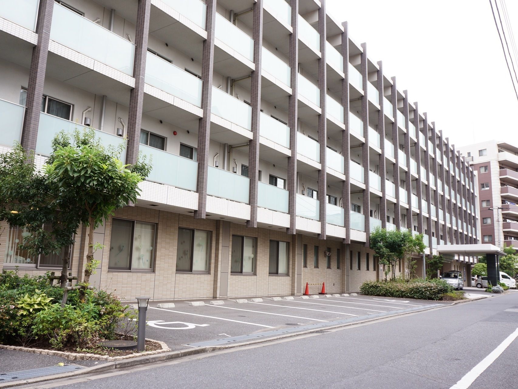 ５階建ての施設はマンションのような外観である。施設前には駐車スペースが確保されている。手入れの行き届いた植栽がある。