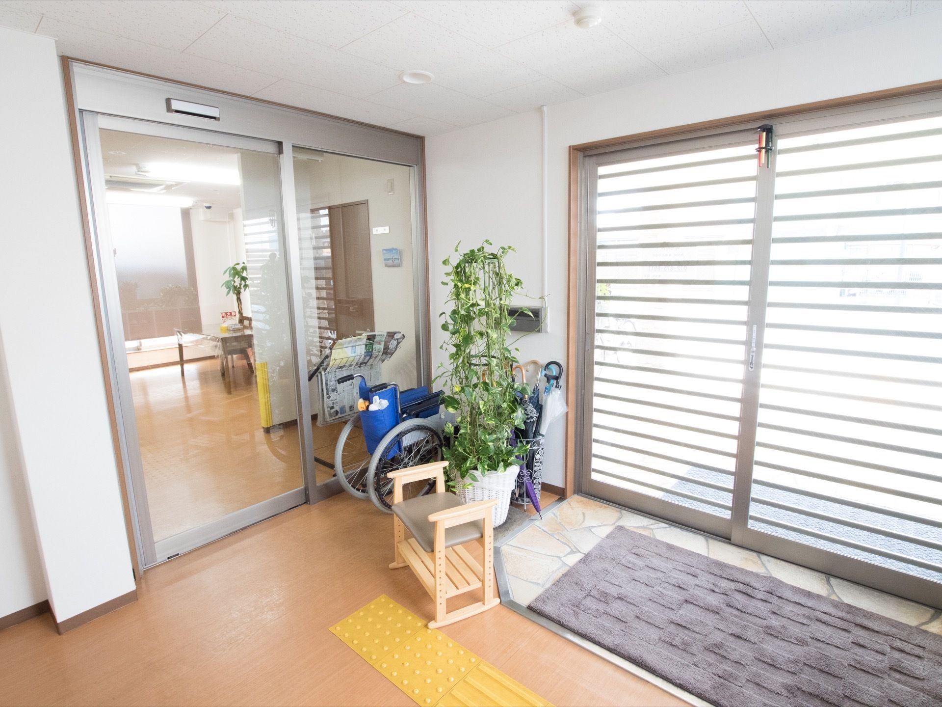 広々とした自動ドアが完備された、明るい玄関である。観葉植物が置かれているほか、車椅子や腰掛椅子も設置されている。