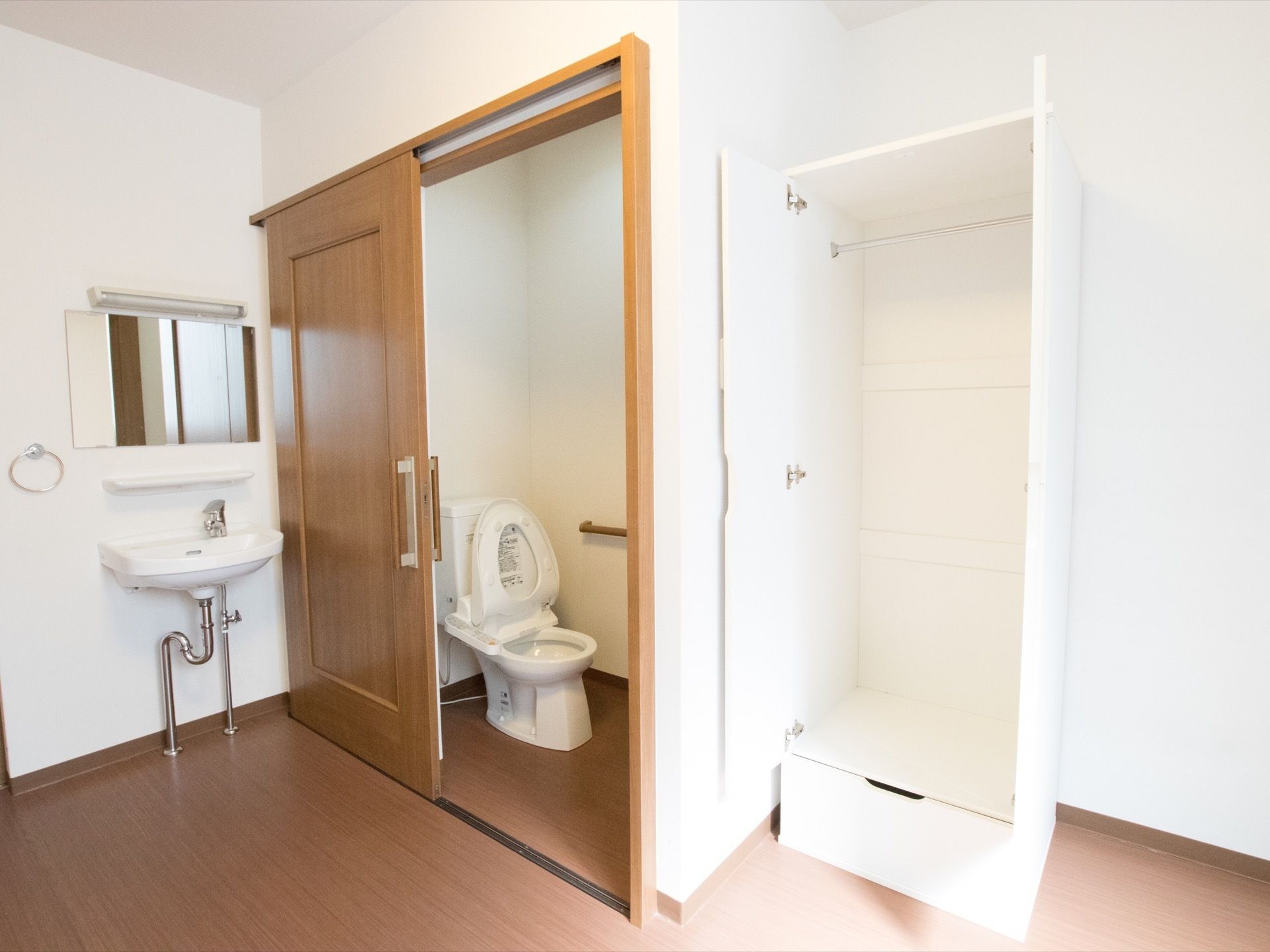 落ち着いた茶色のフローリング部屋である。洗面台やトイレ、白色のスタイリッシュなクローゼットも完備されている。