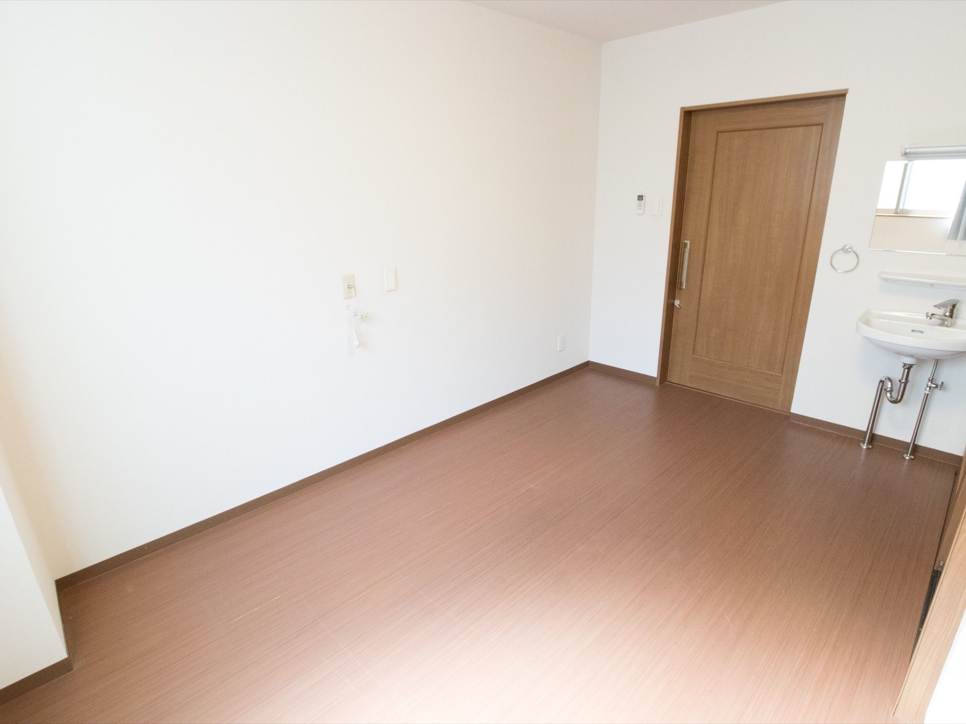壁は白く、建具と床色は落ち着きのあるブラウンで施工されている。居室へ入るとすぐにフットレス仕様の洗面台がある。