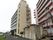 川沿いに道路に面して建っている７階建ての施設である。道路から玄関に向かう入口に黄色の看板が立っている。