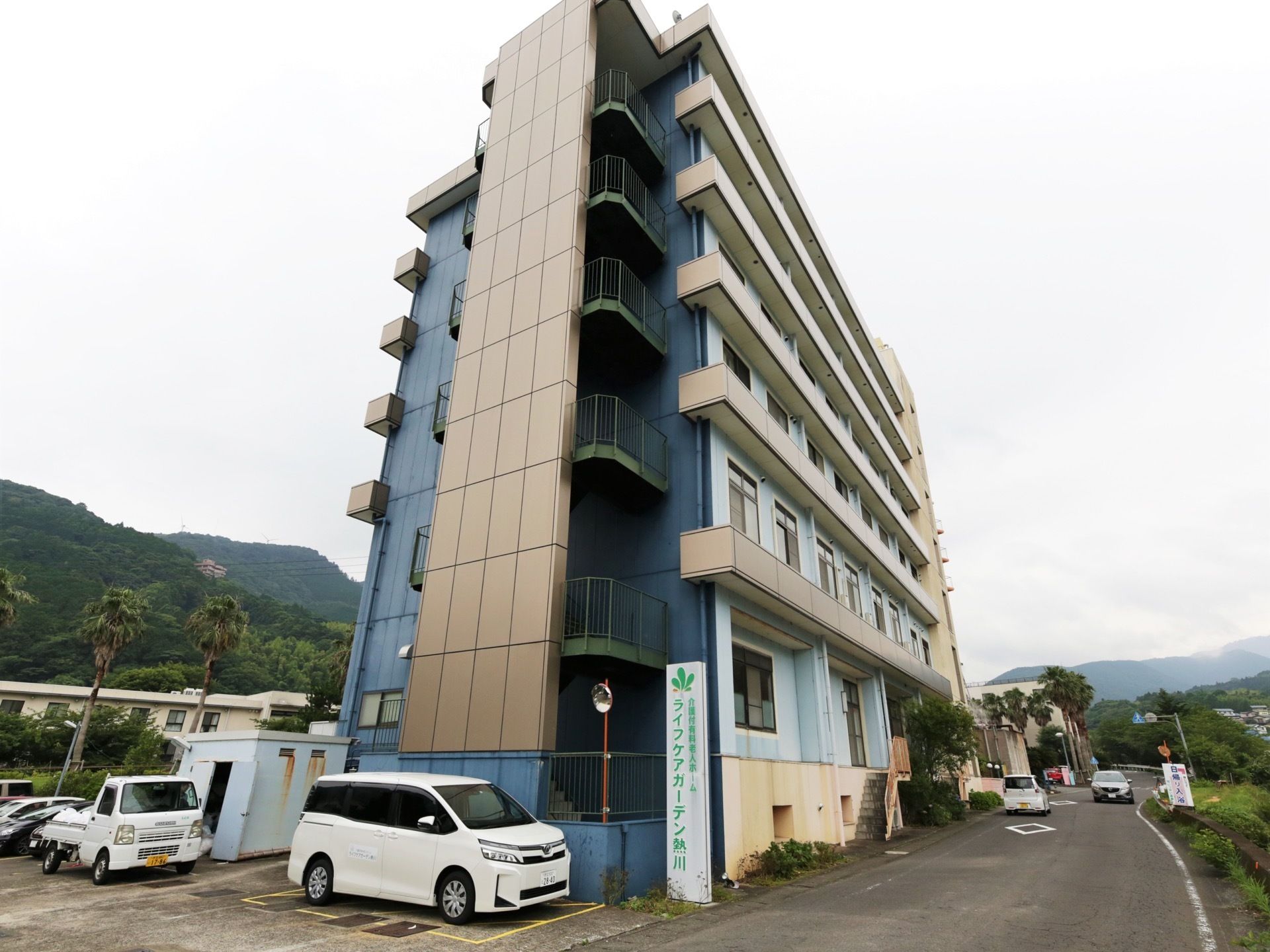 道路沿いに立地している細長い構造の施設である。建物の横に、緑の文字で書かれた縦長の看板が設置されている。