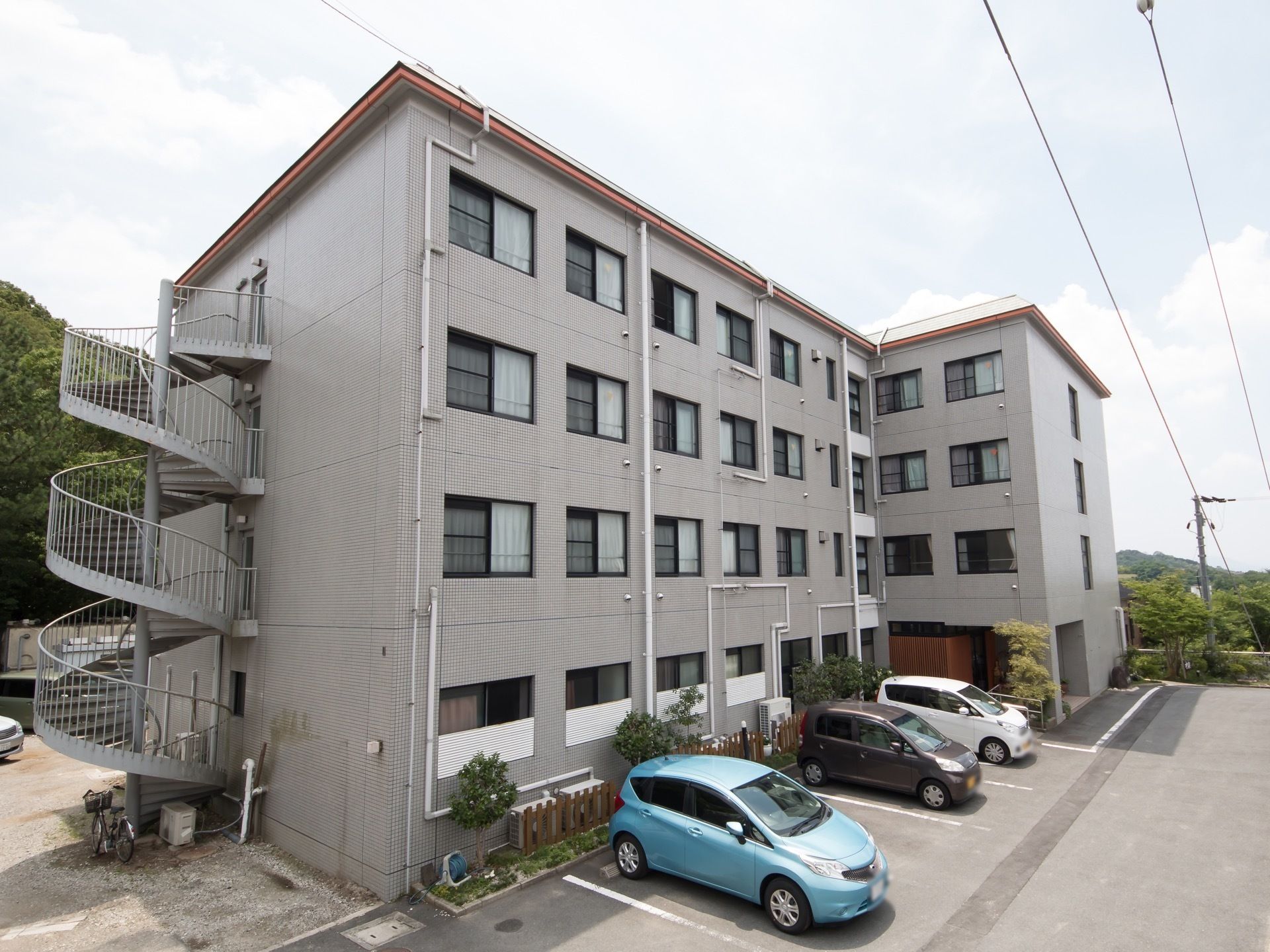 施設はグレーの外壁の大きな建物である。建物の周りには木々が多く植えられており、自然豊かな環境の中で過ごすことができる。