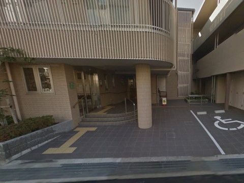 玄関前には車椅子マークが描かれた駐車スペースがある。道路と敷地の境に段差はない。点字ブロックが足元に設置されている。