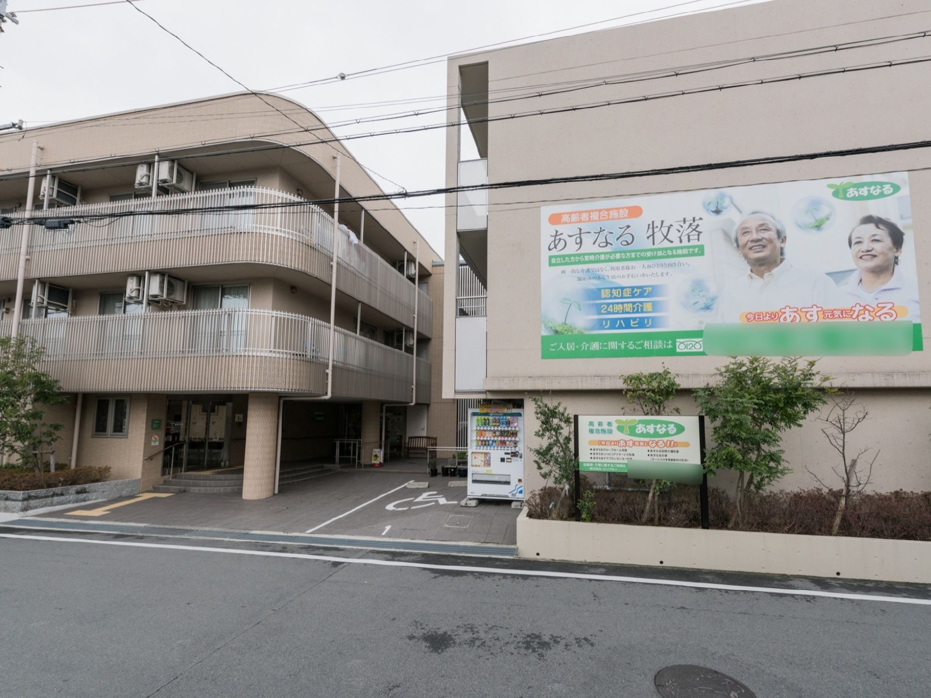 施設は道路に面して建てられている。１階には自動販売機が設置されている。その横には車椅子専用駐車場がある。