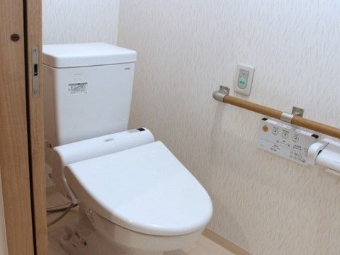 引き戸使用のトイレ。壁に手すりやシャワートイレ用がリモコン設置されている。手すり上部の手がすぐ届く位置に、ナースコールボタンがある。