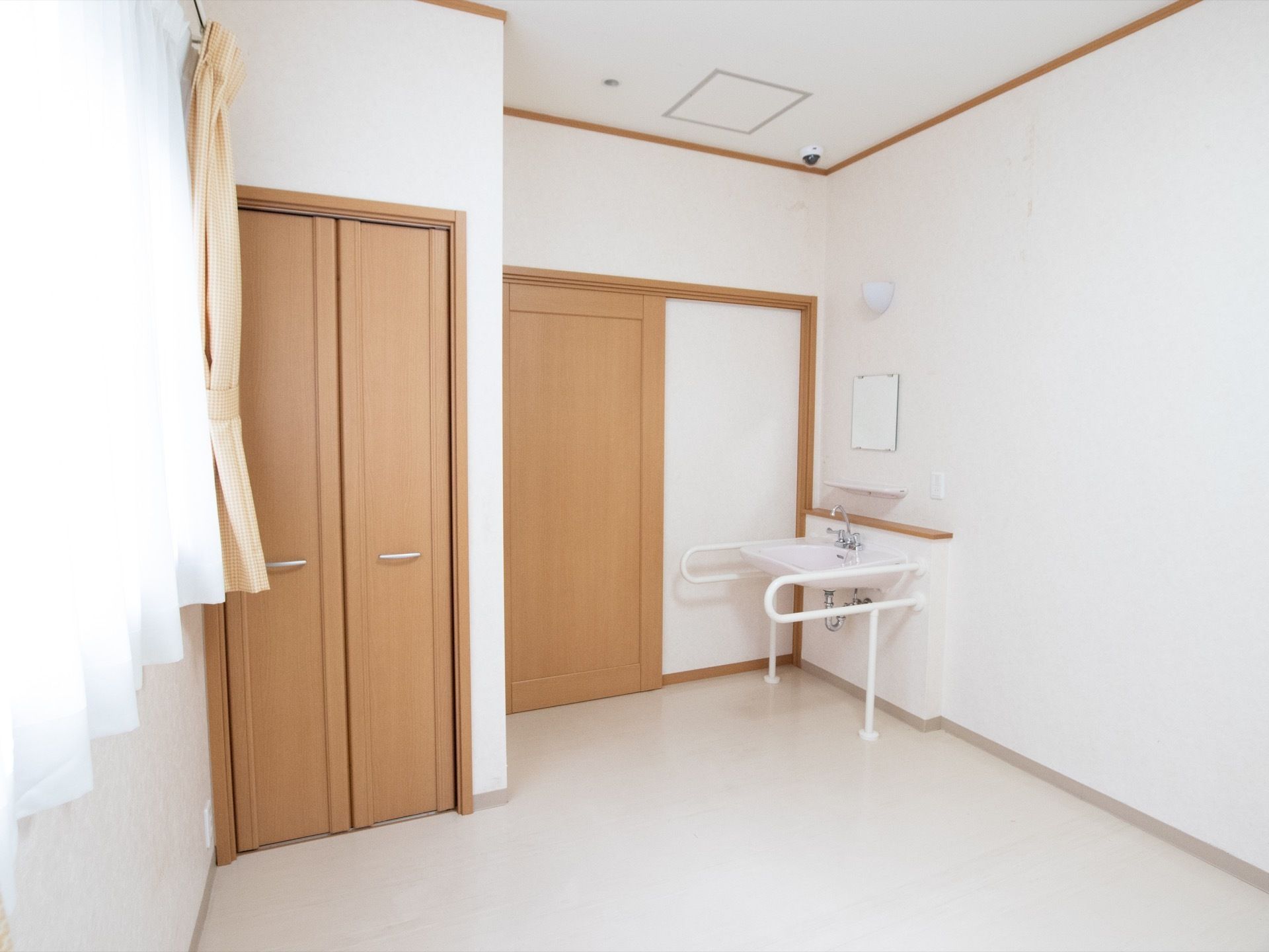 白を基調としたシンプルな居室である。洗面台やクローゼットが完備されており、天井には防犯カメラが設置されている。