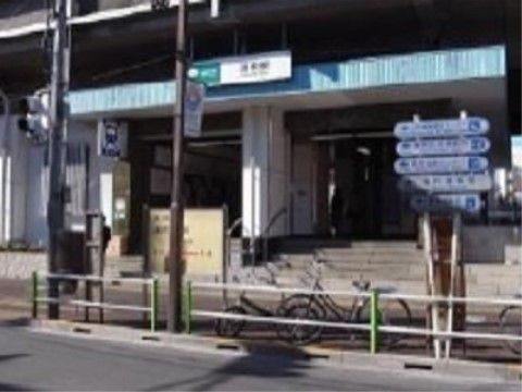 都営地下鉄の駅の入り口周辺である。道路に面した歩道から階段が設置されており、屋根が設けられている。道路には柵があり、標識が建てられている。