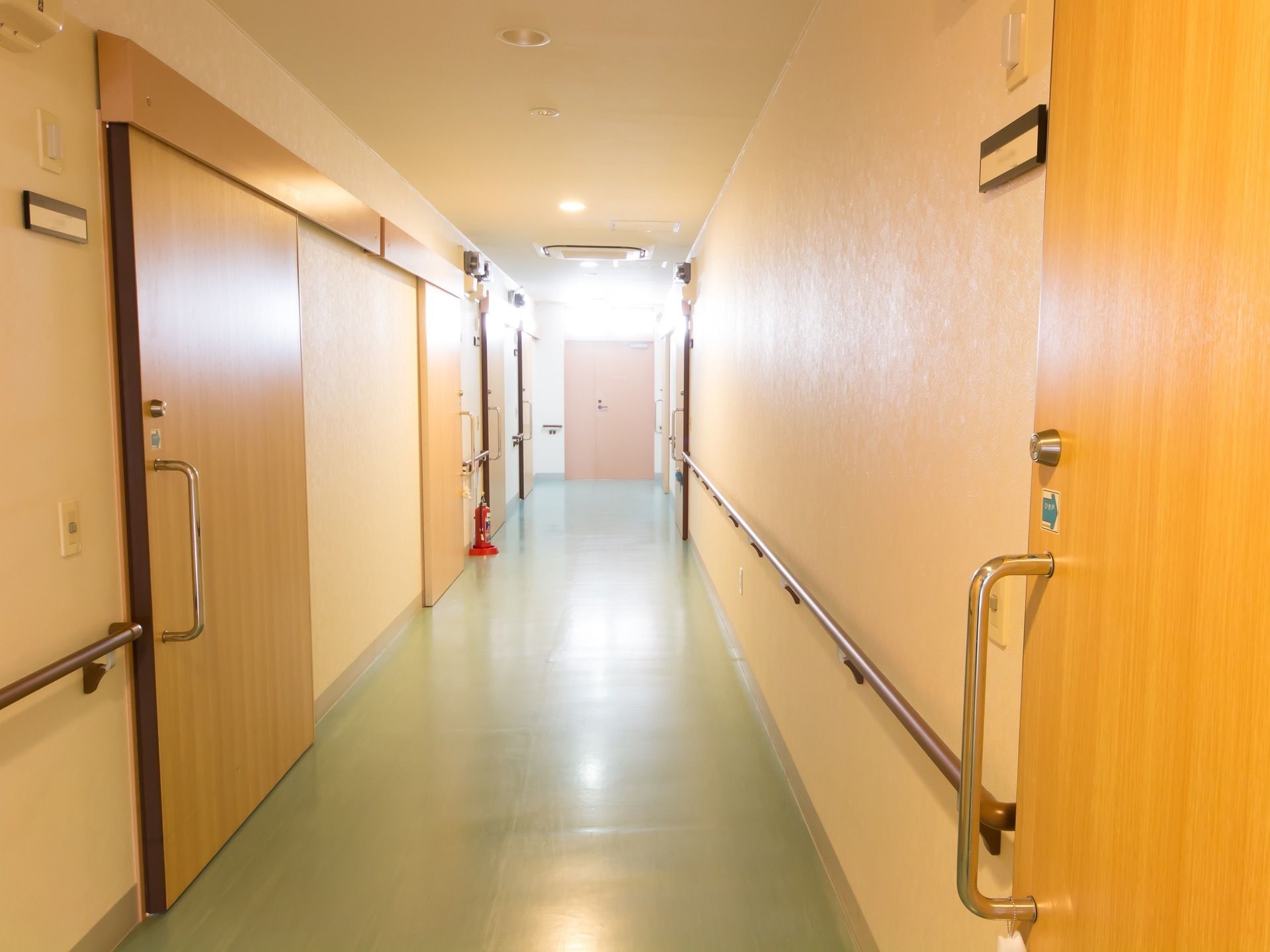 通路はまっすぐと続いている。床は薄緑色で、壁は白色である。壁には長い手すりと部屋の扉が並んでいる。扉は引き戸である。