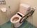 温水洗浄機能付きの便器が設置されたトイレである。そばに可動式の手すりがあり、壁には水流のコントローラーが設置されている。