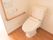 トイレの壁に緊急呼び出しボタンが設置されている。その下から、オレンジ色の玉がついた紐がぶら下がっている。