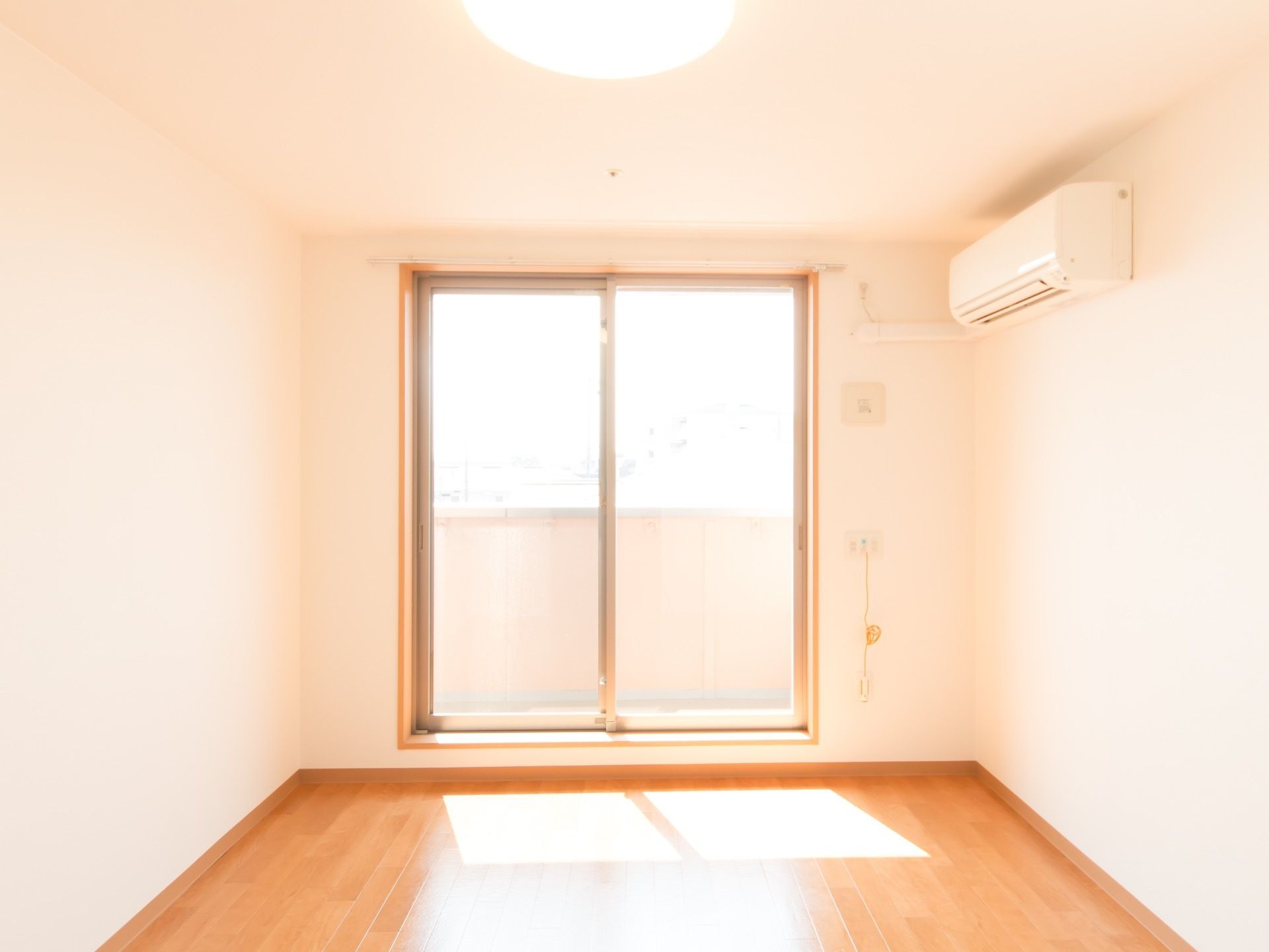 居室に大きな掃き出し窓があり、太陽光が差し込んでいる。バルコニーに出ることができる。エアコンが設置されている。