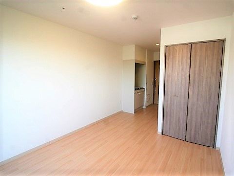 清潔感のある白い壁とフローリングの床の居室には、両開きのクローゼットとミニキッチンが設置されている。
