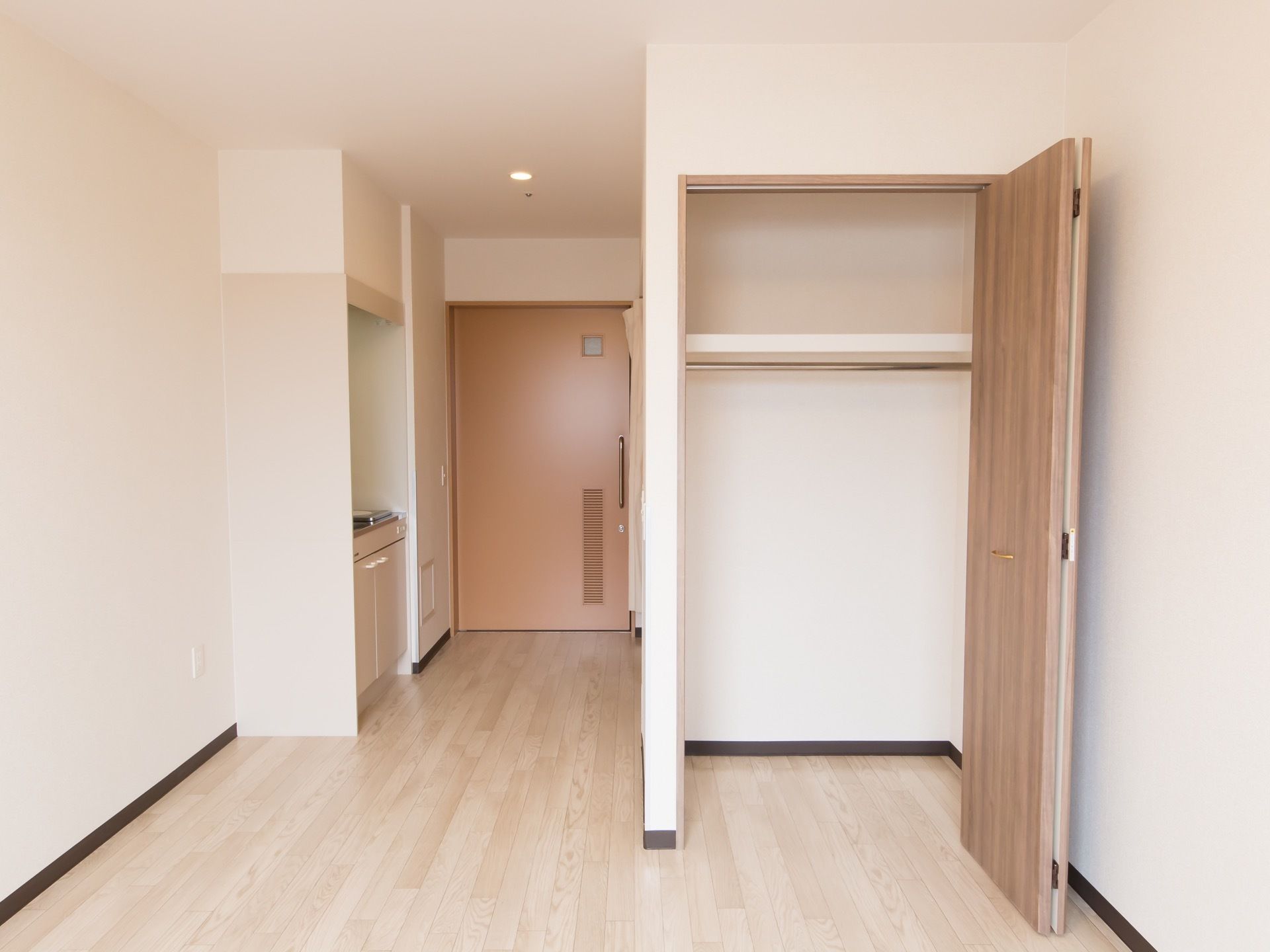 淡いピンク色の扉の居室で、フローリングの床である。作り付けのクローゼットやキッチン、トイレが備わっている。