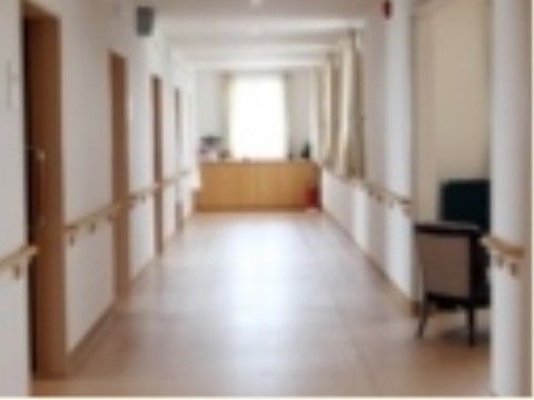 幅が広い廊下の両側の壁には、居室ドアが並び、間の壁には手すりが付いている。壁の一部が凹んでおり、椅子が置かれている。突き当りには窓がある。