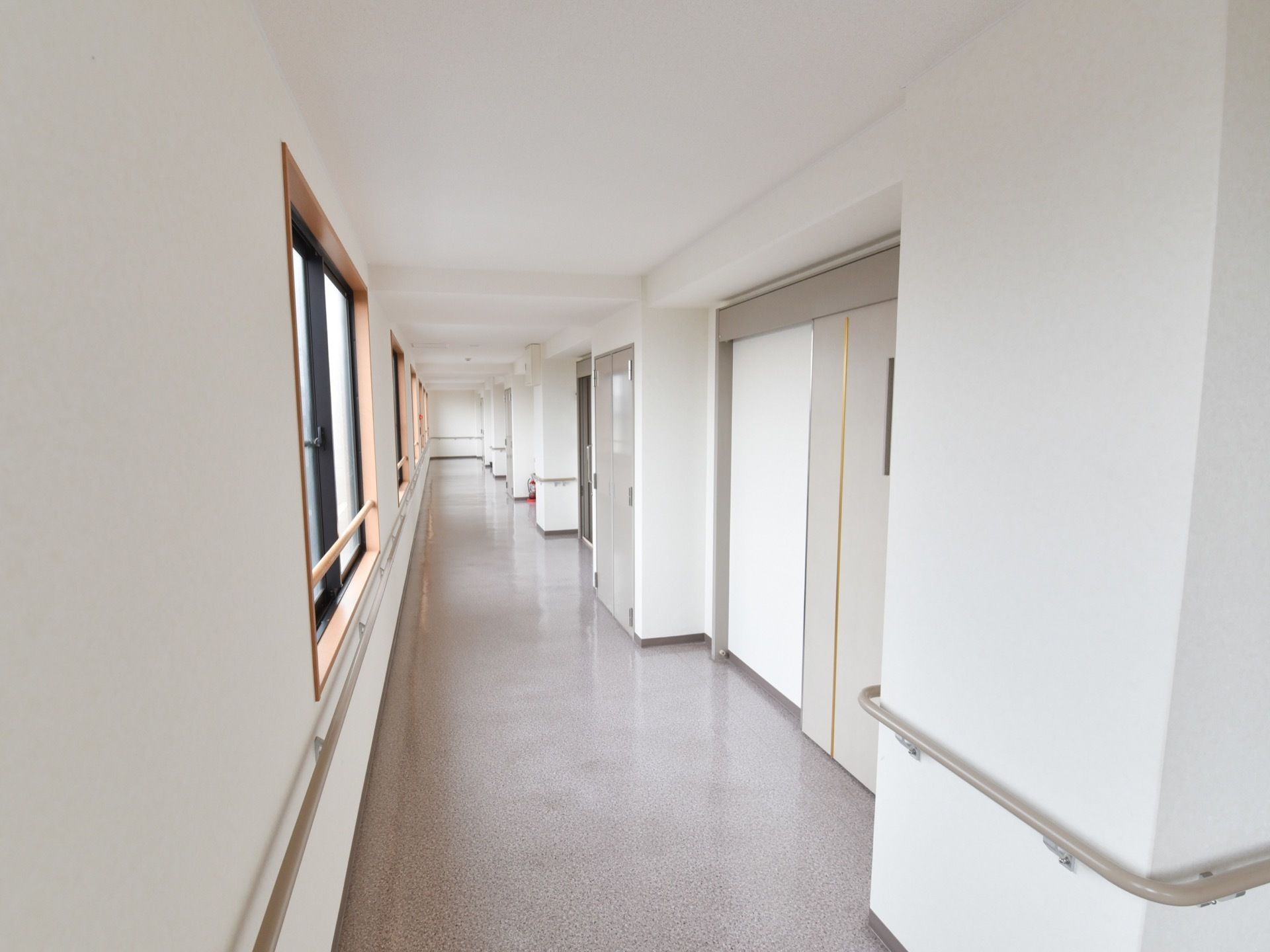 窓に面した広々とした通路。白い壁とグレーの扉がスッキリとしたデザインになっている。壁には手すりが設置されている。