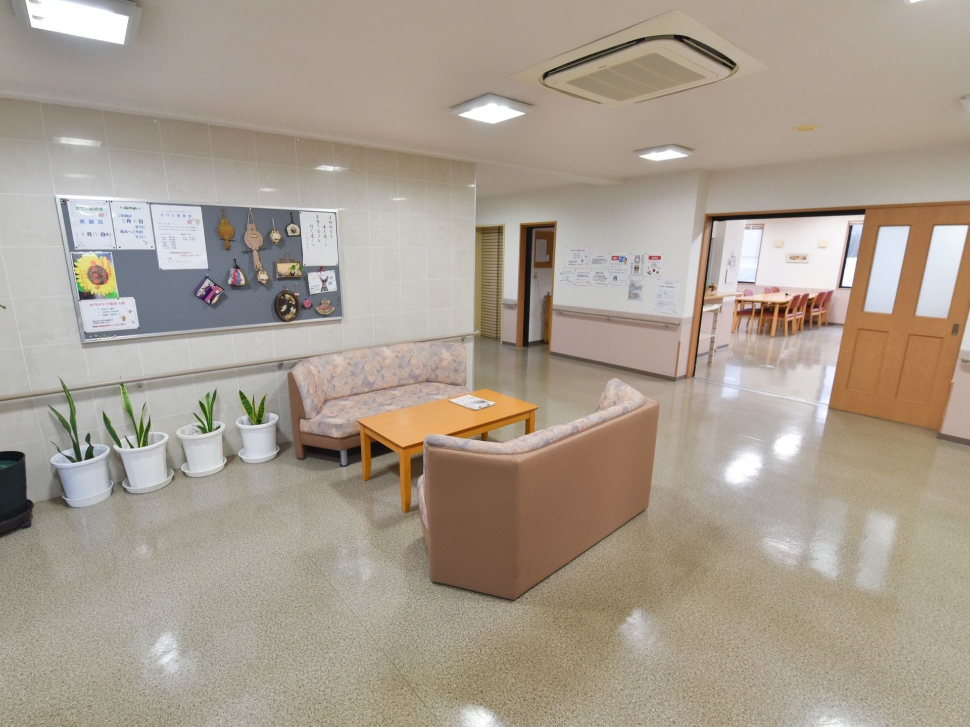 広々としたホールに設けられている休憩スペース。ソファとテーブルが置かれている。壁の掲示板には各種お知らせが貼られている。