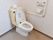 清潔感があるトイレである。温水洗浄機能付きの便座が設置されている。グレーを基調とした壁にＬ字型の手すりが取り付けられている。