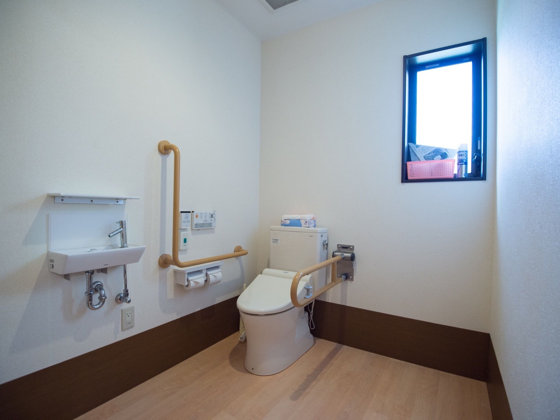 小窓に清掃用品や小物が置かれている。温水洗浄便座付きのトイレが設置されており、壁には手すりが備えつけられている。
