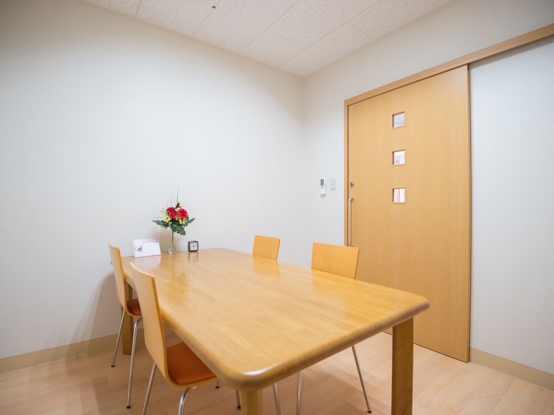 白を基調とした部屋にテーブルと椅子が置かれている。テーブルの上には花や小物が飾られている。扉は引き戸になっている。