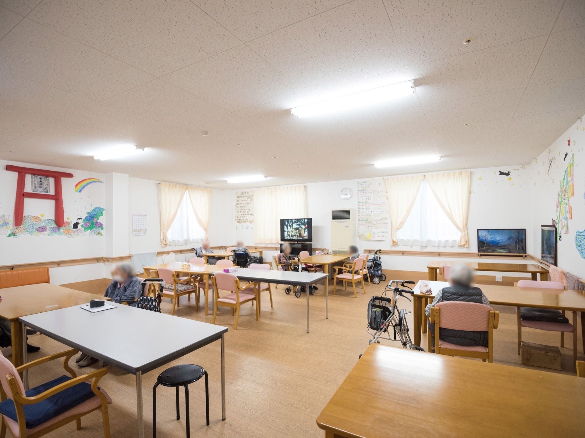 広々とした食堂には窓が多く設置され、明るく開放的な空間となっている。テーブルが間隔を開けて多数設置され、入居者様が一緒に過ごしている。