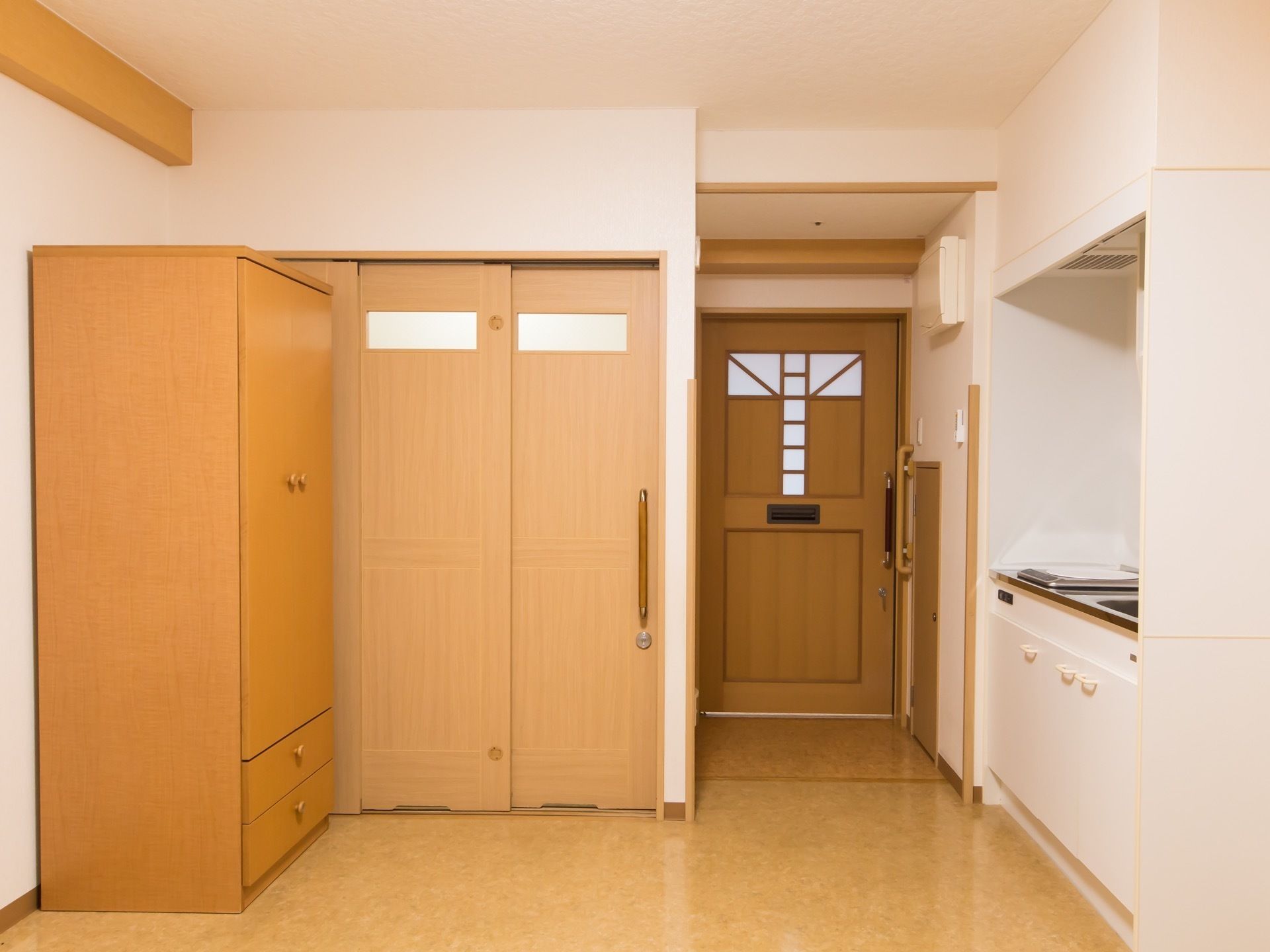 居室のドアは木製のおしゃれなデザインをしており、室内には電磁調理器付きのキッチンや大容量の収納タンスなどがある。
