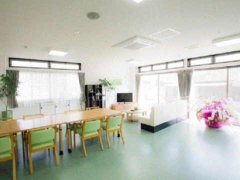 鮮やかなグリーンの床に広々としたダイニングテーブル、椅子が置かれている。採光を取り入れたデザインで明るく快適である。