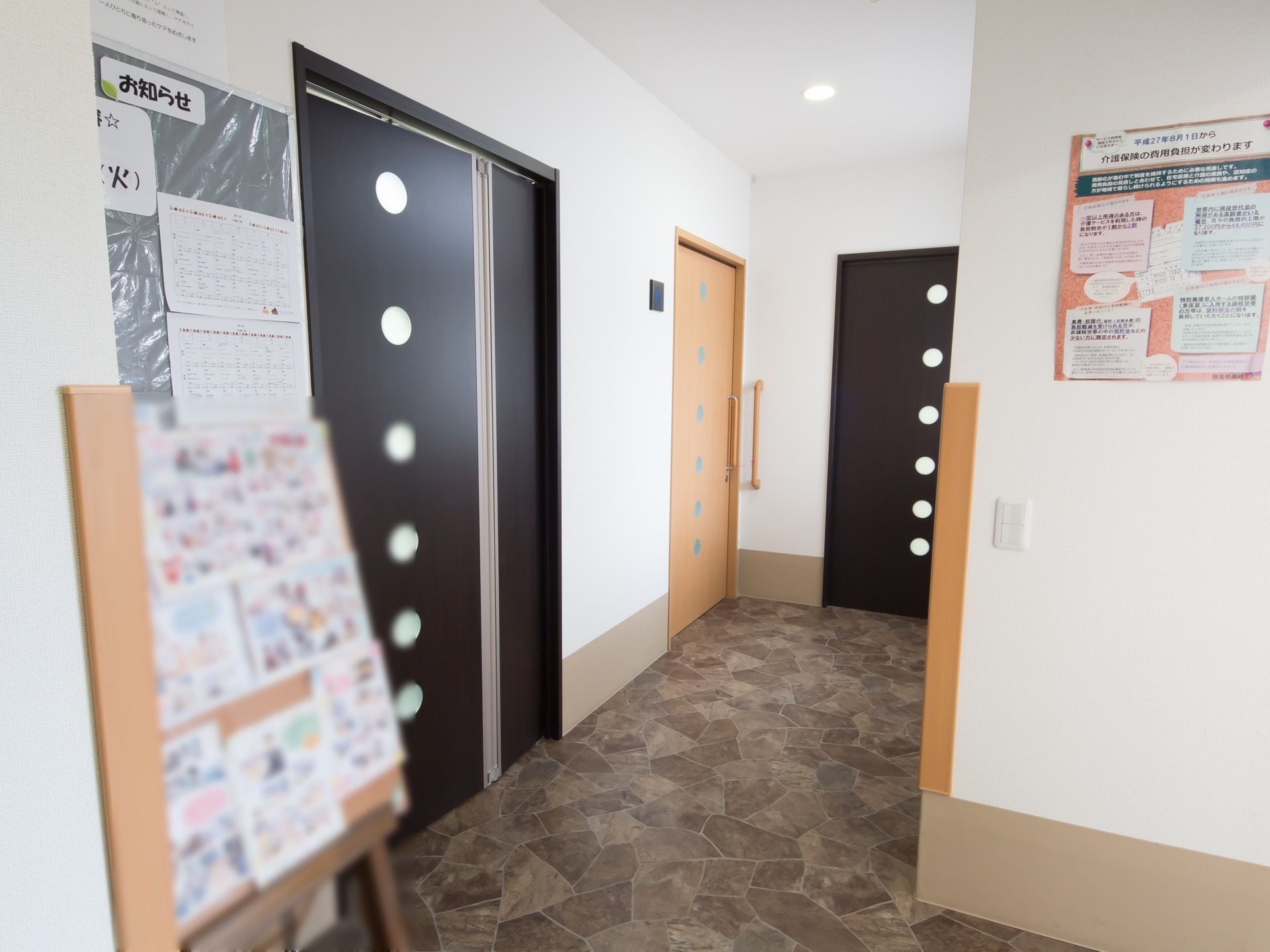 明るく幅の広い廊下である。壁には、お知らせボードが設置されている。扉の横には、I型手すりが取りつけられている。