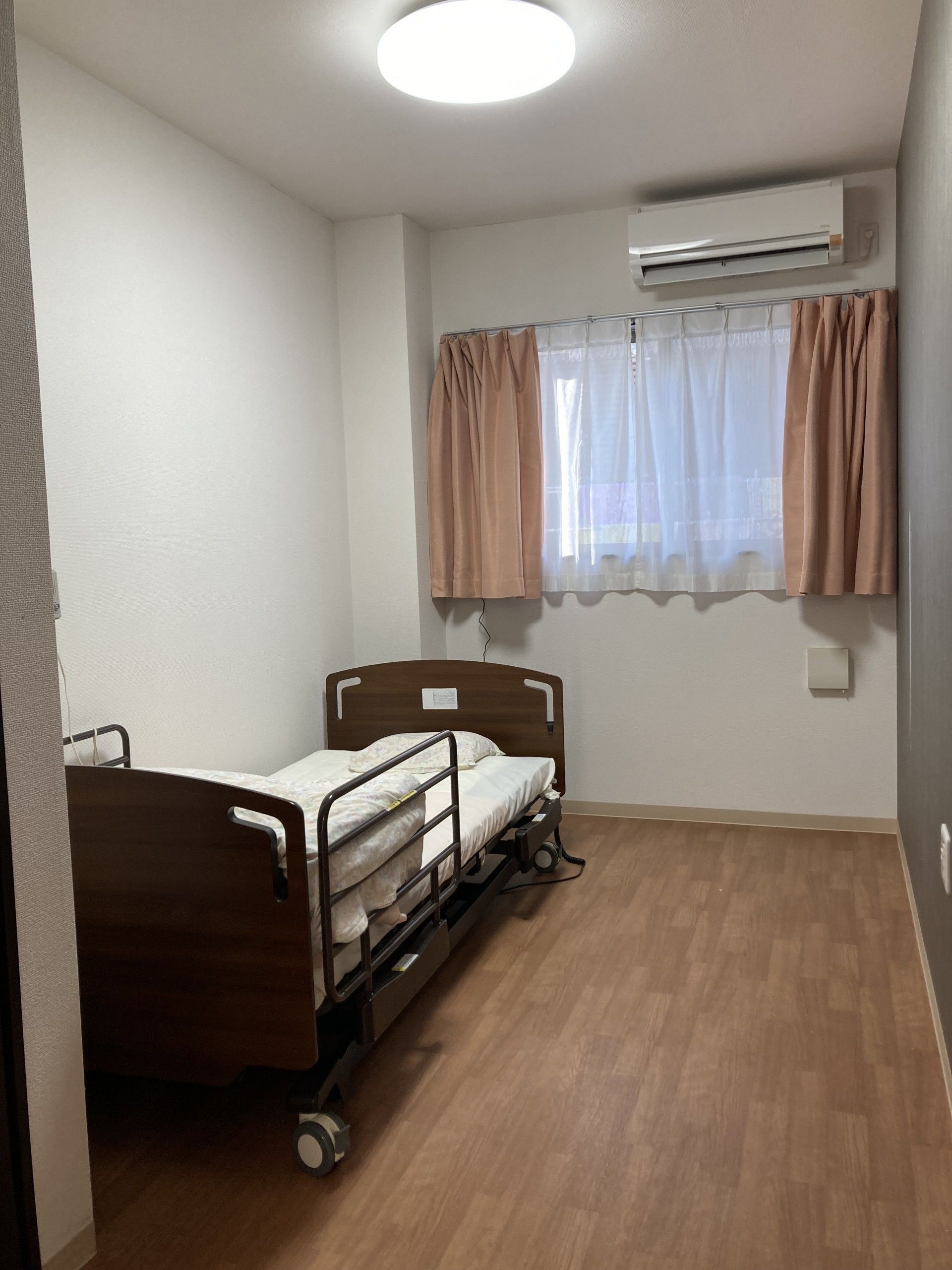 明るい居室の腰窓には黄緑色のカーテンとレースが設置されている。入居者様は明るさに応じて遮光することができる。
