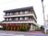 3階建ての建物には2階以上に細かい柵のベランダフェンスが設置されている。前面には生け垣があり、樹木が植えられている。