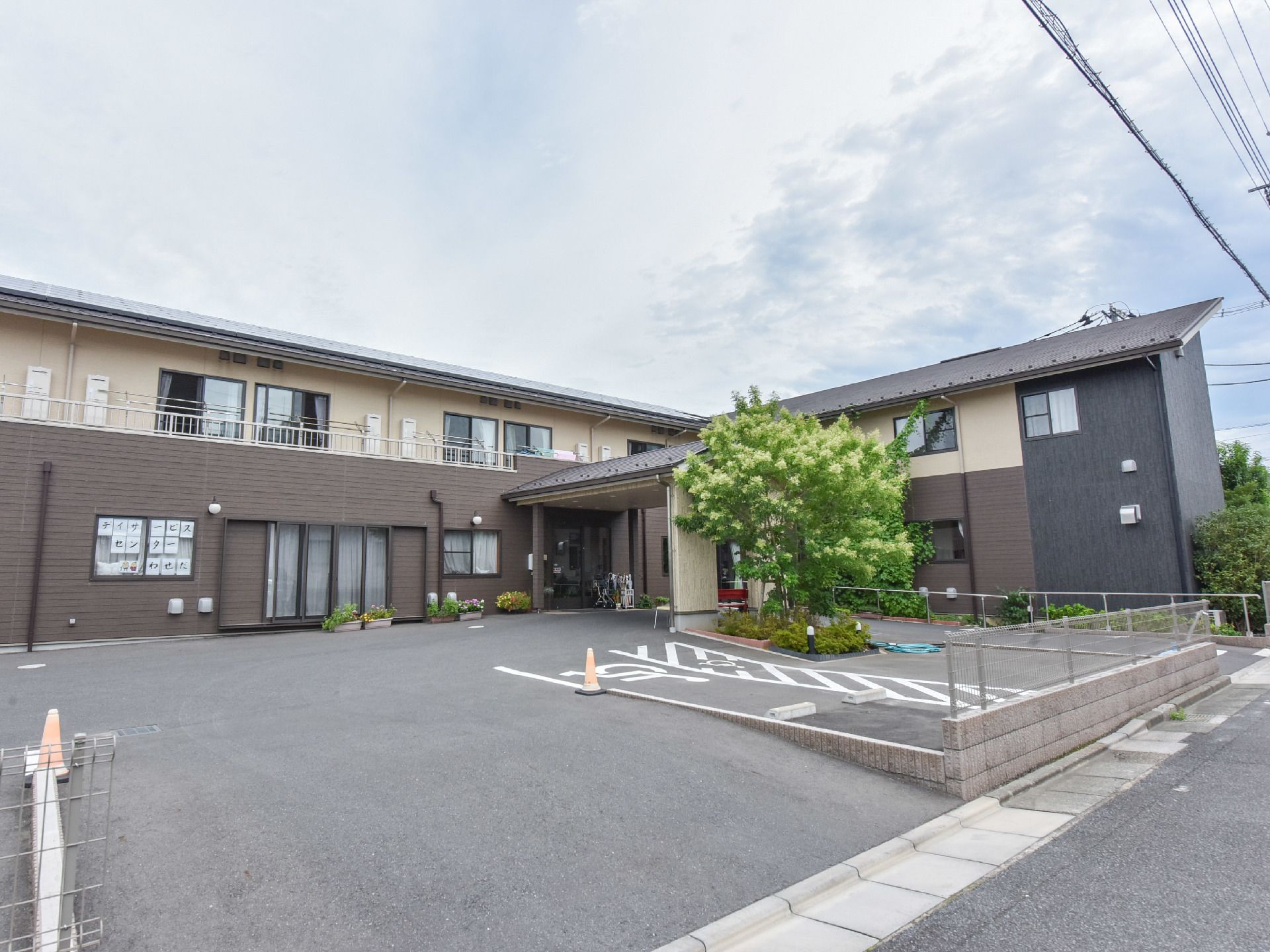 施設の建物は落ち着いた色の2階建てになっている。建物と隣接する道路との間には、複数台停められ駐車場がある。