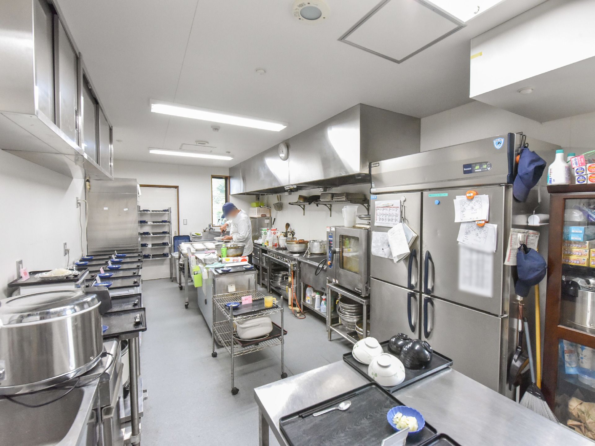 調理場はきれいに整理整頓されている。大型の業務用の冷蔵庫や炊飯器が置かれ、配膳台には沢山のお膳が並んでいる。