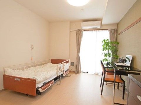 居室は、広めの間取りになっている。介護ベッドやナースコール、エアコンが完備されている。壁際には、椅子とテーブルが置かれている。
