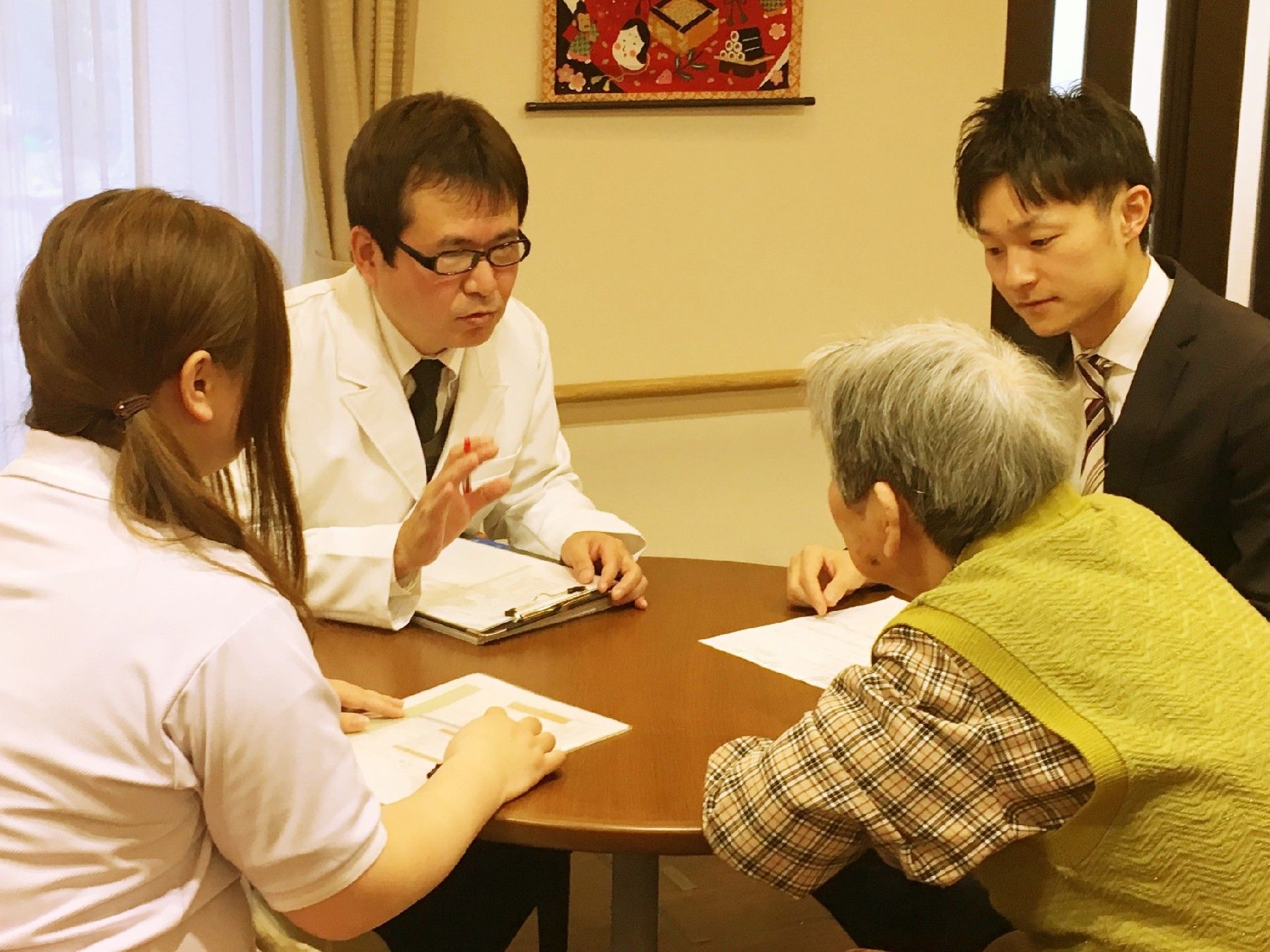 白衣を着て眼鏡をかけた男性が、女性入居者に何かを説明している様子