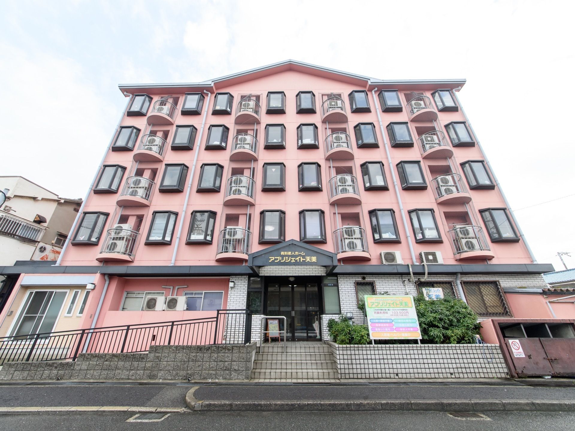 ５階建てで壁はピンク色である。各居室の出窓が道路側に面している。玄関前は中央に階段があり、左側にスロープが設置されている。