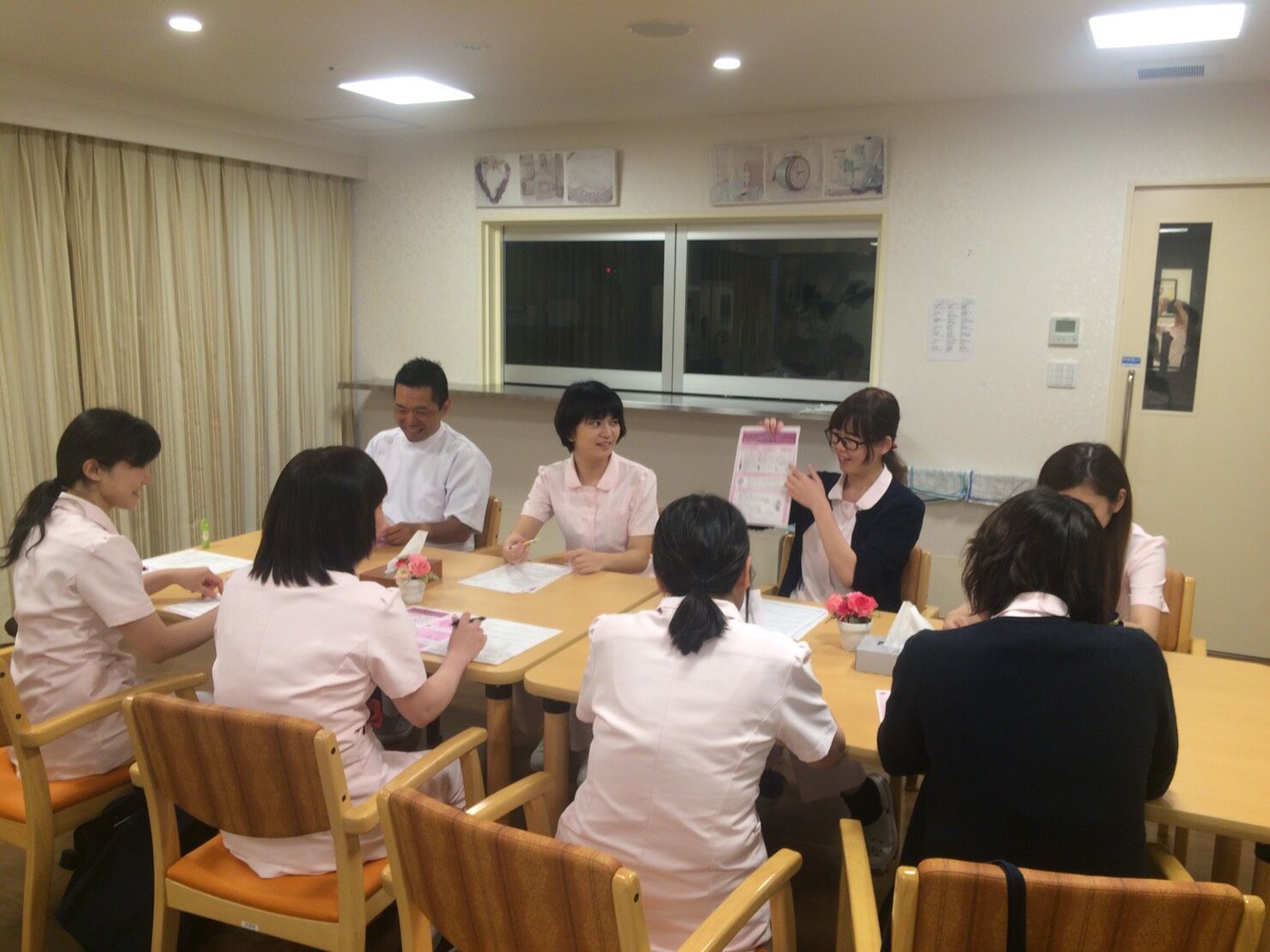 手に持った書類について説明する女性スタッフを笑顔で見つめるスタッフたち