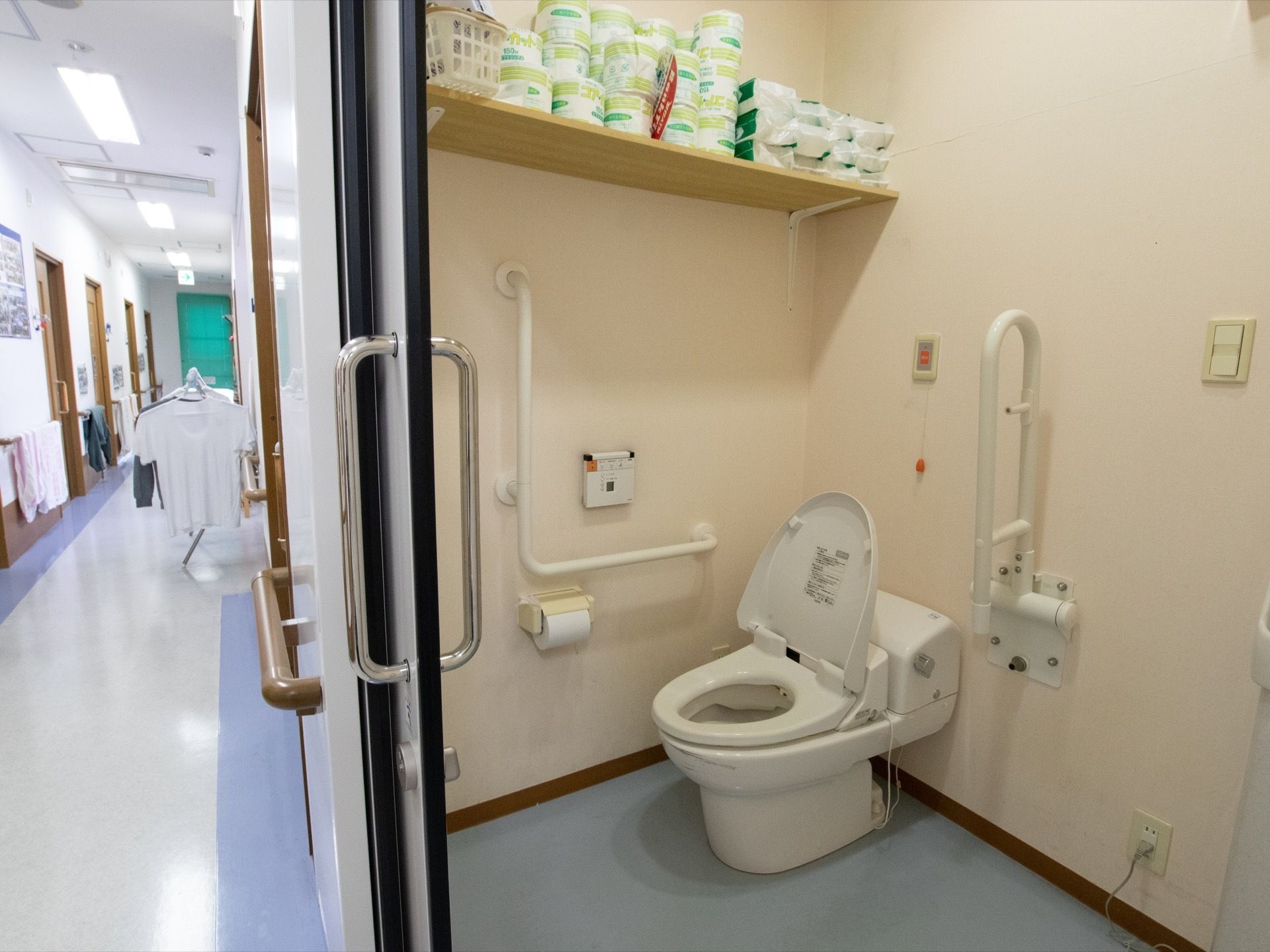 トイレ上部の壁に木製の棚が取り付けられており、トイレットペーパーやペーパータオルなどの予備が多数置かれている。