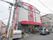 街中に建てられた施設で、グレーの外壁に赤色がアクセントとなっており、バリアフリーの玄関の上には施設名が大きく記載してある。