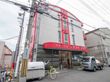 街中に建てられた施設で、グレーの外壁に赤色がアクセントとなっており、バリアフリーの玄関の上には施設名が大きく記載してある。